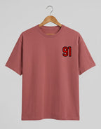 91 Varsity Left Chest graphic t-shirt on CORAL unisex classic crew soft-touch 180 GSM cotton, bold red varsity 91 left-chest pocket print signature, black outline varsity number, minimalist placement subtle distinctive, classic crew neckline timeless, unisex regular fit flattering, pre-shrunk bio-washed maintains shape
