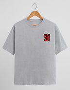 91 Varsity Left Chest graphic t-shirt on GREY unisex classic crew soft-touch 180 GSM cotton, bold red varsity 91 left-chest pocket print signature, black outline varsity number, minimalist placement subtle distinctive, classic crew neckline timeless, unisex regular fit flattering, pre-shrunk bio-washed maintains shape
