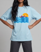 Sunset Boat graphic t-shirt on BABY BLUE unisex 100% cotton crew neck, vibrant high-quality serene sunset boat scene, artistic flair beach design, DTG print 300 DPI, 180 GSM breathable soft fabric