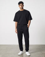 A man wearing Tribe Neo 91 black cotton fleece joggers with a drawstring waist and ribbed cuffs in a regular fit.