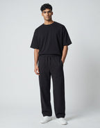 Male model wearing Tribe Neo 91 black wide-leg cotton sweatpants with an elastic drawstring waist and front pockets.