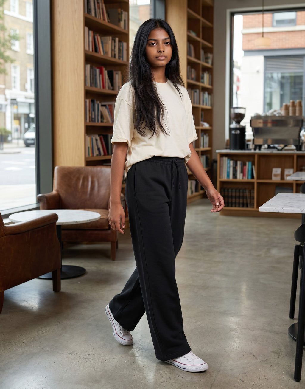 A model wearing Tribe Neo 91 black wide-leg cotton sweatpants with an elastic drawstring waist in a casual cafe setting.