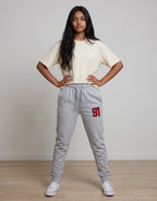 Tribe Neo 91 unisex grey cotton fleece joggers with red 91 graphic on thigh, worn by a woman with a cream t-shirt.