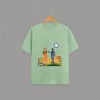 Tribe Neo 91 sage green cotton unisex t-shirt featuring a whimsical robot and human graphic print on a wooden hanger.